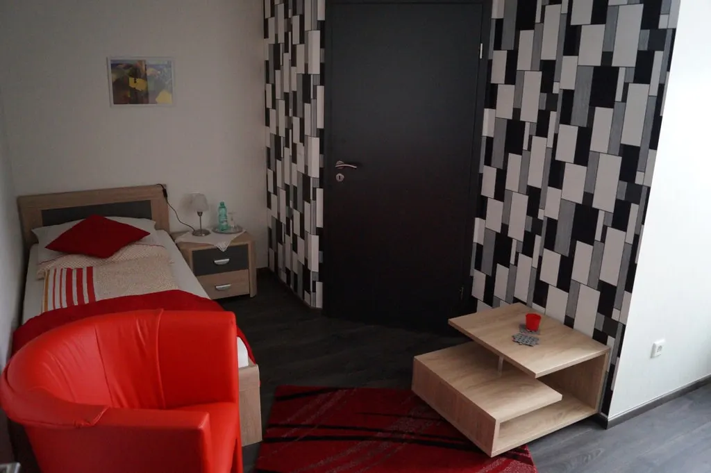 Einzelzimmer mit rotem Sessel, Couchtisch und gemusterter Wand